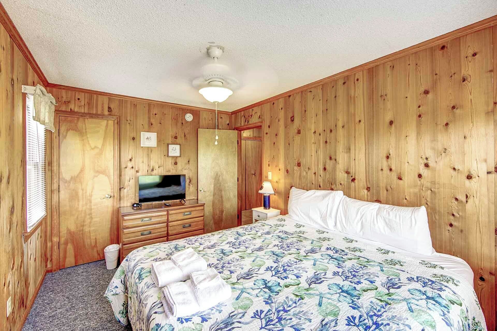 A wooden-paneled room with a bed, a TV, a dresser, and a nightstand.