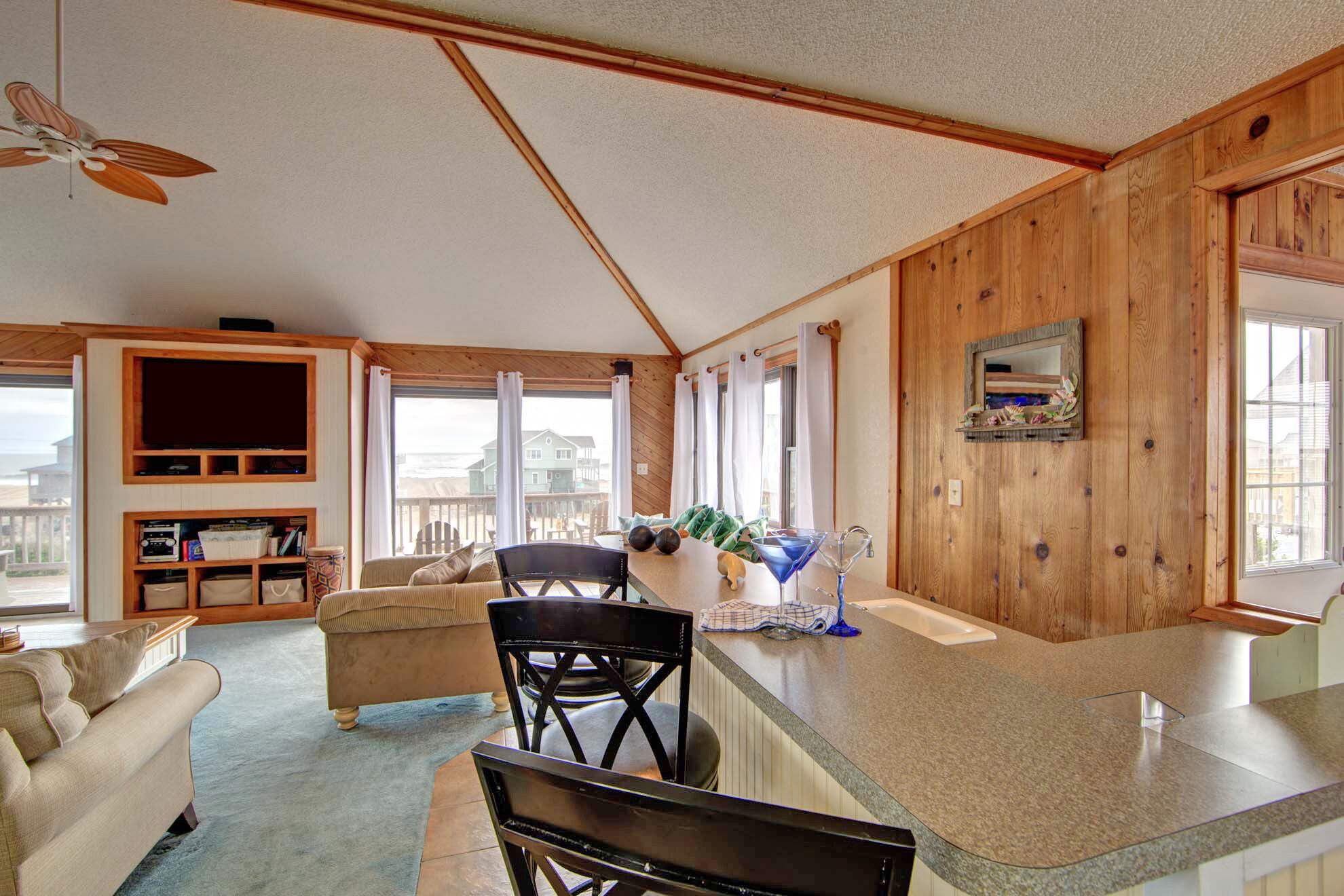 A spacious living area with a large window, a ceiling fan, and a kitchen counter with a sink and decorative items.