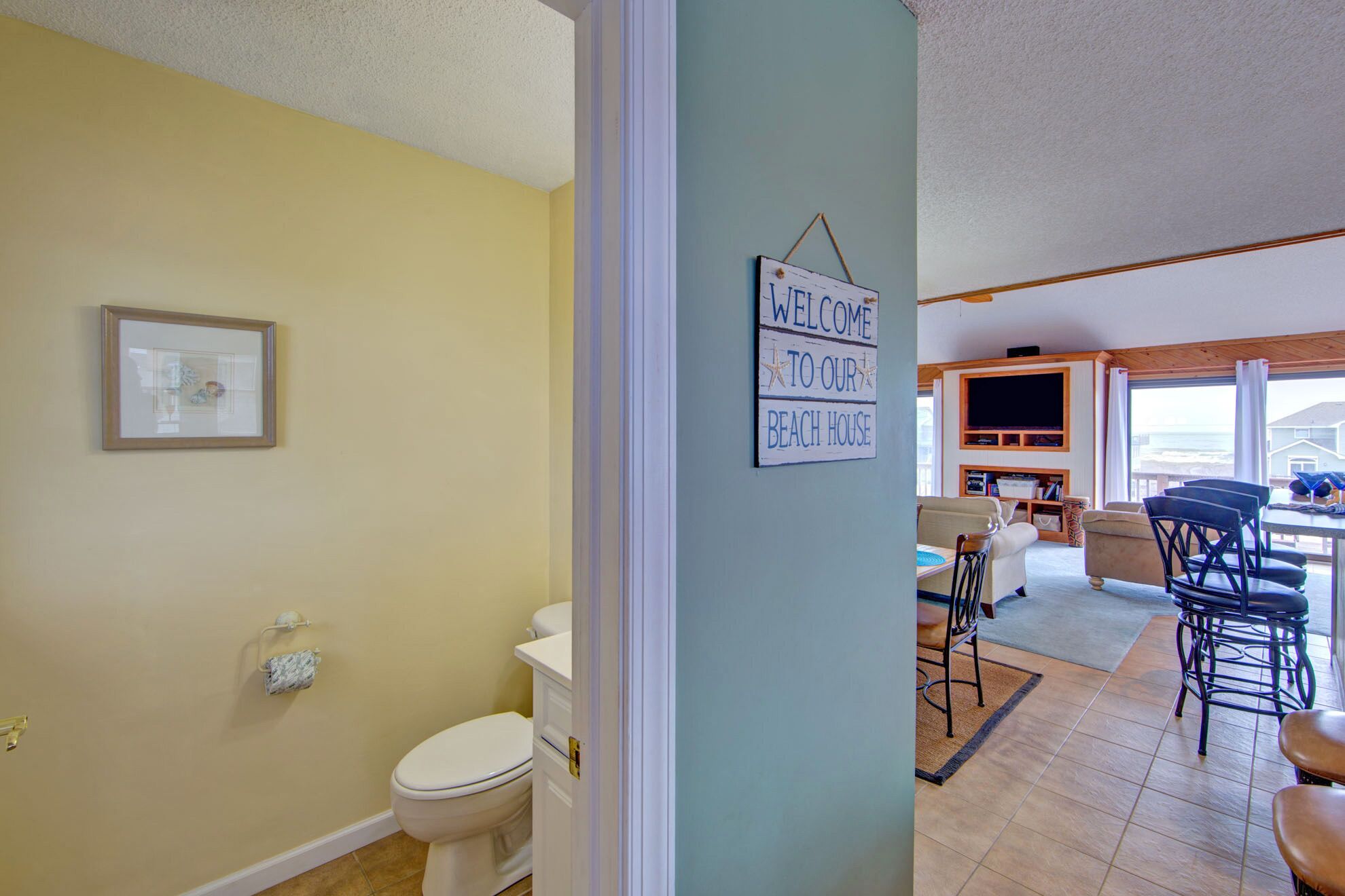 A bathroom with a toilet, a framed picture on the wall, and a welcome sign.