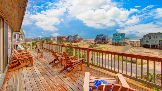 A wooden deck with chairs and a view of beach houses. - Semi-Oceanfront, Beach Access, Hot Tub & Pool Table (Avon)
