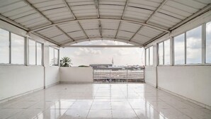An empty, spacious balcony with a metal roof and large windows, offering a view of the cityscape.
