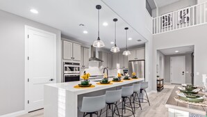 Une cuisine moderne dotée d’un îlot central, de tabourets de bar, d’appareils électroménagers en acier inoxydable, de luminaires suspendus et offrant une vue sur l’étage supérieur.