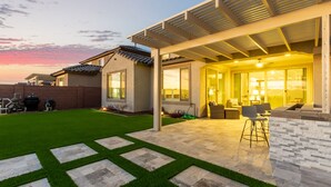 Une maison moderne dotée d’un patio, d’un espace salon extérieur abrité et d’une pelouse bien entretenue.