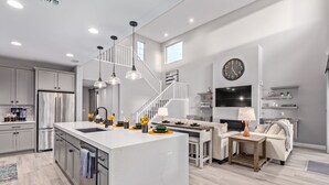Une cuisine moderne dotée d’un îlot central, un coin repas avec un canapé, une cheminée et un salon avec une télévision et des objets décoratifs.