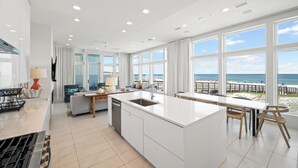 Une cuisine moderne dotée d’un grand îlot central, de meubles blancs et offrant une vue sur la plage.