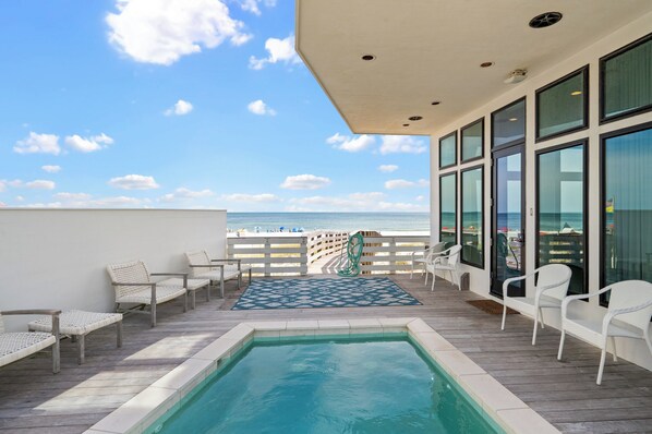 A poolside area with a view of the beach, deck chairs, and a small pool.