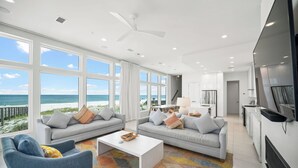 Un salon spacieux doté de grandes fenêtres, d’un ventilateur de plafond et offrant une vue sur la plage.
