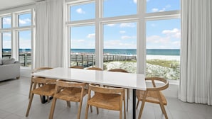 Un espace repas avec une grande table et des chaises, de grandes fenêtres offrant une vue sur l’océan, ainsi qu’une vue sur la plage et la jetée.