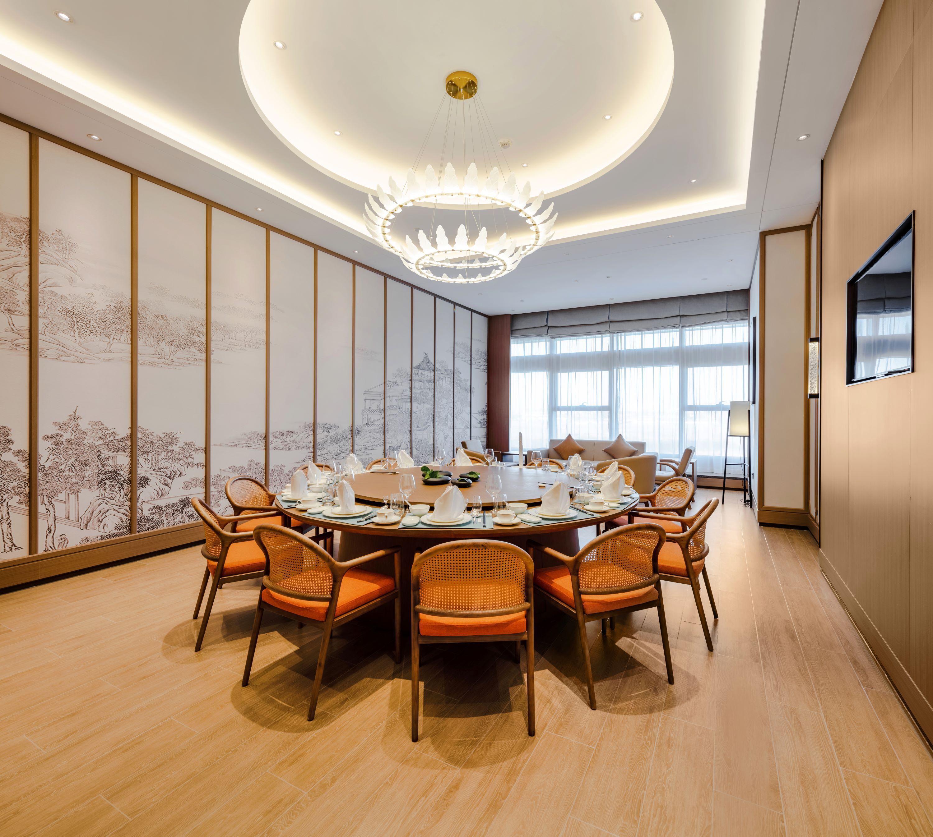A dining area with a round table set for a meal, surrounded by wicker chairs with orange cushions.