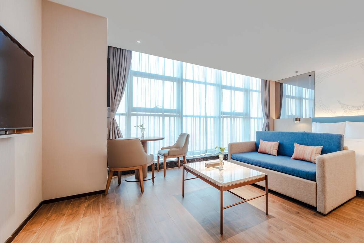 A modern hotel room with a large bed, a sofa, a coffee table, and a TV.