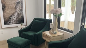 Ett rum med en grön soffgrupp, ett litet sidobord med en vas med blommor och en inramad tavla på väggen.