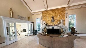A spacious living room with a fireplace, a large sofa, and two decorative horse statues. - Bay-Front Dream Mansion and Guest House -20 minutes to Destin beaches on 4 acres (Freeport)