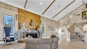A spacious living area with a fireplace, a large armchair, a sofa, and a staircase. - Bay-Front Dream Mansion and Guest House -20 minutes to Destin beaches on 4 acres (Freeport)