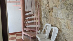 Una escalera en espiral con barandillas de metal, sillas de plástico blanco y una pared de piedra.