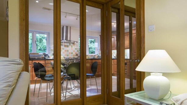 A room with a bed, a white lamp, and a view of a kitchen through a glass door. - Merewood Lodge (Windermere)