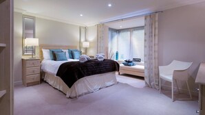 A modern bedroom with a large bed, bedside tables, a chair, and a window with curtains. - Merewood Lodge (Windermere)