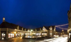 A historic town square at night with illuminated buildings and a central fountain. - Wynford (Ambleside)
