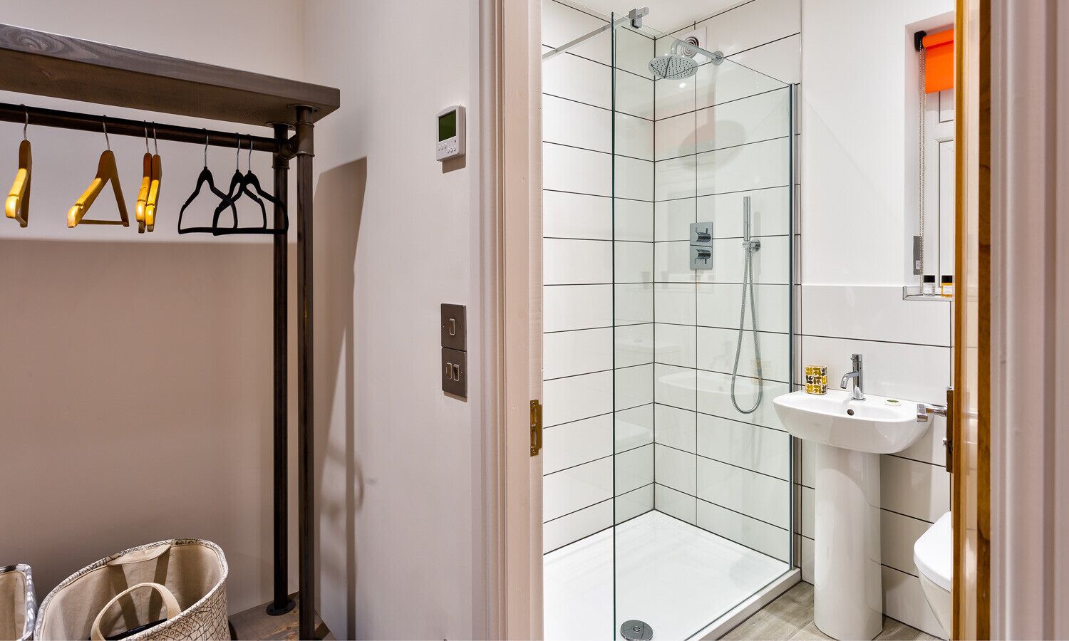 Ein modernes Badezimmer mit einer Duschkabine aus Glas, einem weißen Waschbecken und einem Hakenleisten-Handtuchhalter.