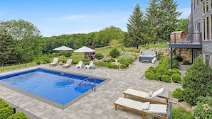 A swimming pool with lounge chairs and umbrellas, surrounded by a landscaped garden and a stone wall. - Tower House | Heated Pool, Sauna, Hot Tub + Views (Galena)