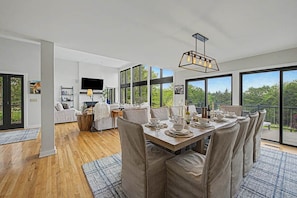 A modern dining area with a large table set for six, a sofa, and a TV in the background.