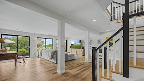 A spacious living area with a staircase, large windows, and a dining area. - Tower House | Heated Pool, Sauna, Hot Tub + Views (Galena)