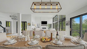 A dining room with a large table set for a meal, a chandelier, and a view of the outdoors. - Tower House | Heated Pool, Sauna, Hot Tub + Views (Galena)
