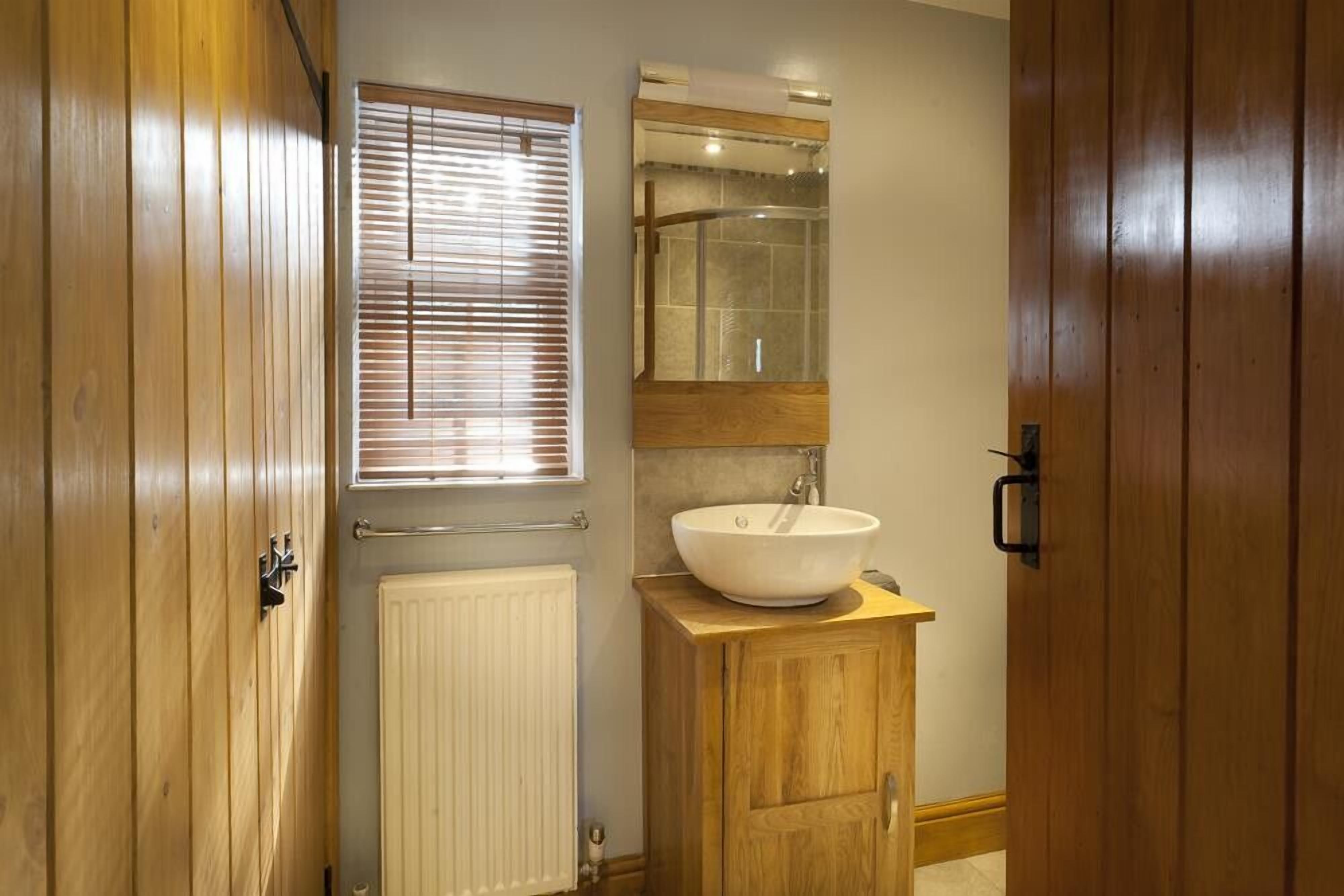 A bathroom with wooden cabinets, a white sink, a mirror, and a window with blinds.