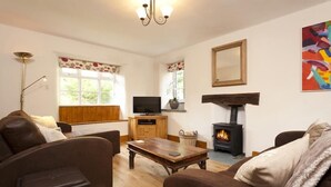 A cozy living room with a fireplace, wooden furniture, and a television. - Wythebank (Coniston)