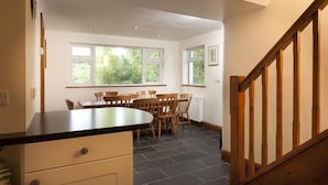 A kitchen with a dining table and chairs, large windows, and a wooden staircase. - Wythebank (Coniston)