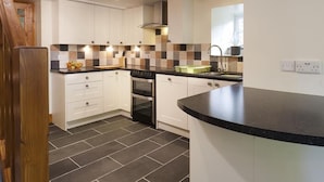 A modern kitchen with white cabinets, a black countertop, and a tiled backsplash. - Wythebank (Coniston)