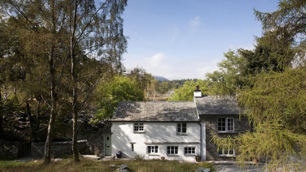 A white house with a stone roof, surrounded by trees and a stone wall. - Wythebank (Coniston)