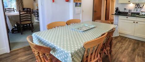 Uma área de refeições com uma mesa coberta por uma toalha de bolinhas, rodeada por cadeiras de madeira.