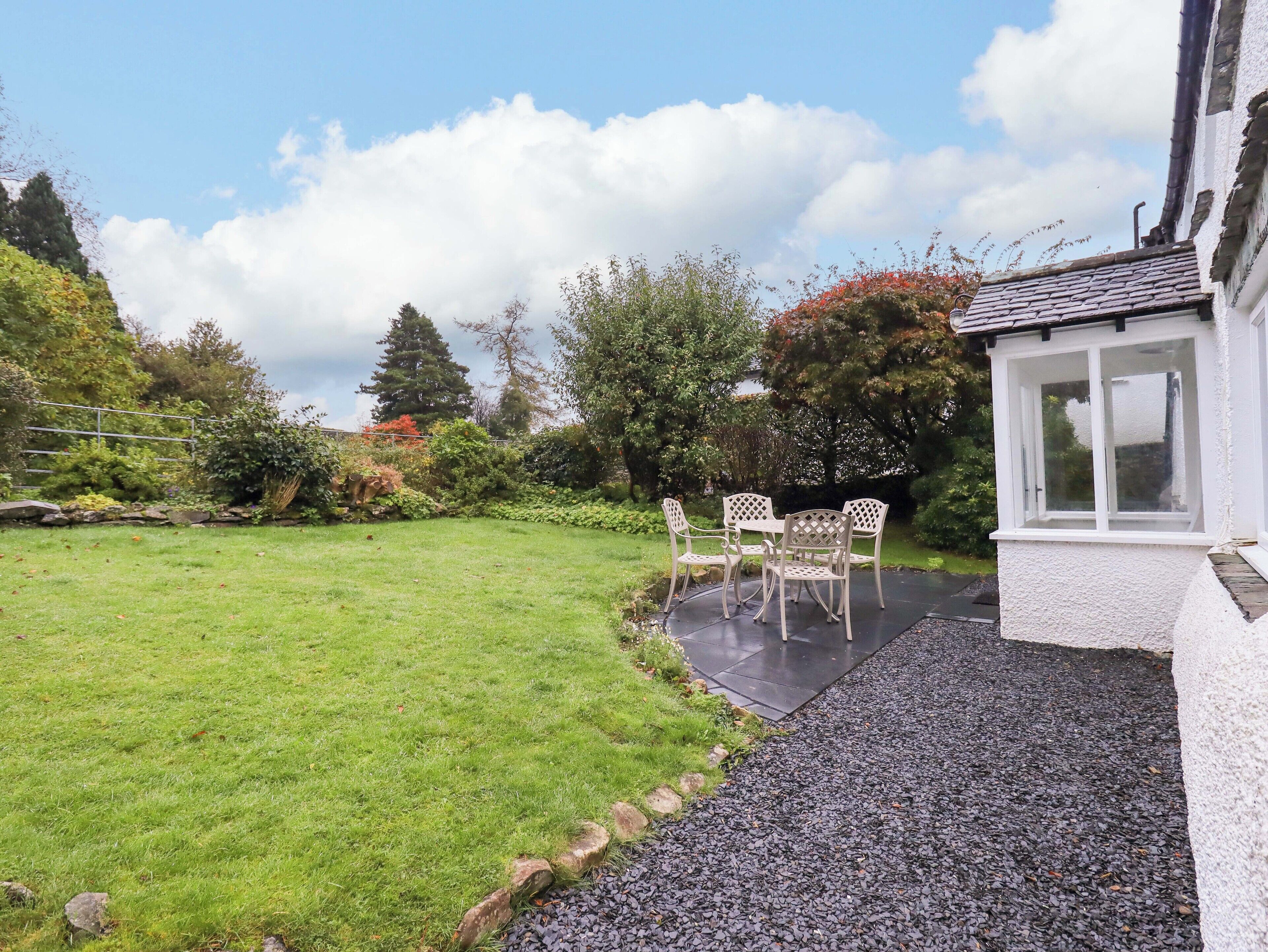 A garden with a patio table and chairs, surrounded by a well-maintained lawn and various plants.