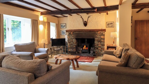 A cozy living room with a stone fireplace, wooden beams, and comfortable seating. - Ecclerigg Old Farm (Windermere)