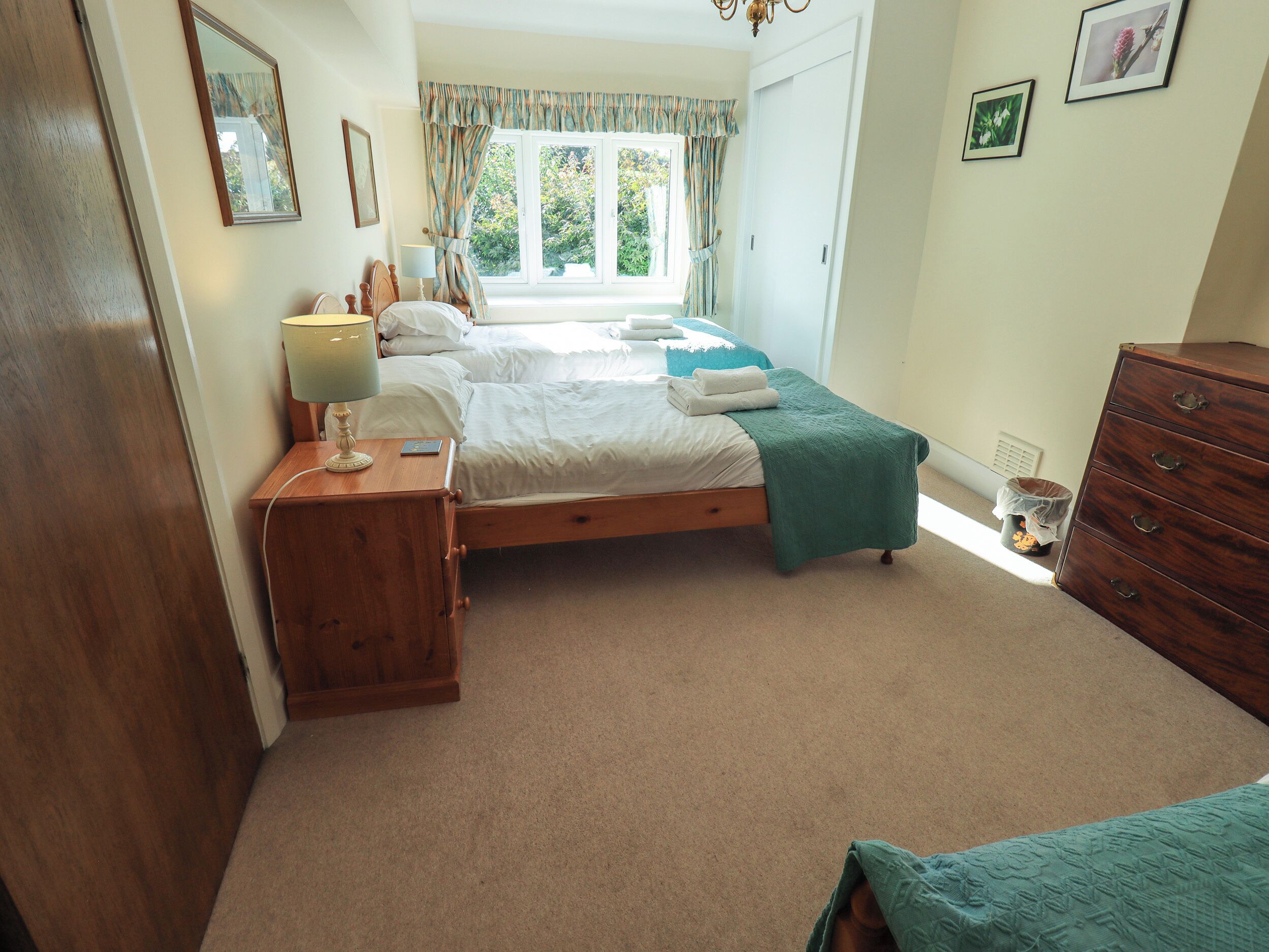 A bedroom with a double bed, a bedside table with a lamp, a dresser, and a window with curtains.