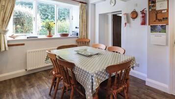 Een eetkamer met een tafel, overdekt met een tafelkleed met stippen, omringd door houten stoelen.