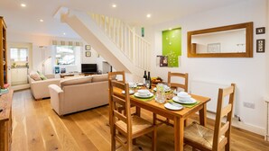 Un coin repas avec une table en bois dressée pour quatre personnes, entourée de chaises en bois. Un escalier mène à l’étage supérieur.