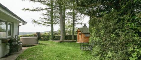 A backyard with a wooden playhouse, a hot tub, and a lawn.