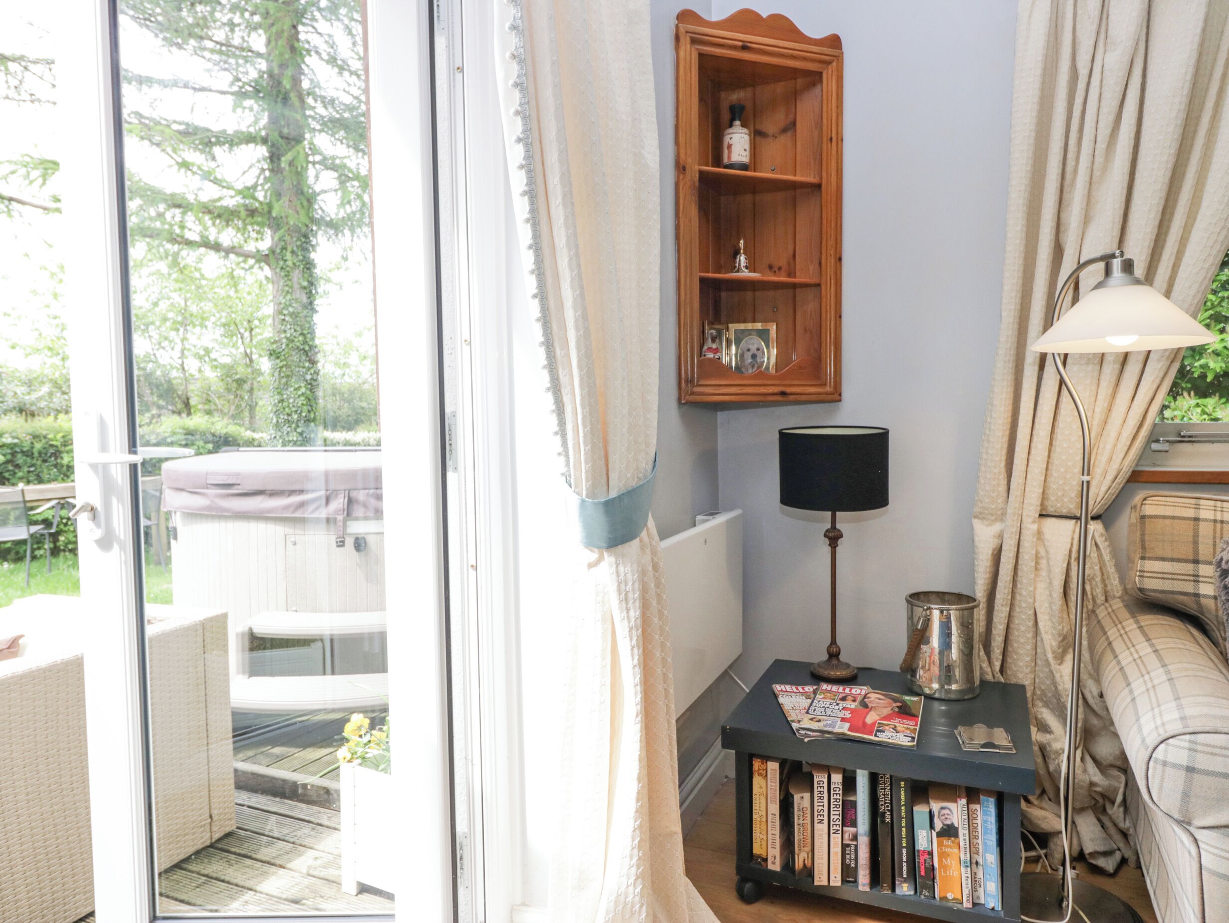 Ein gemütliches Wohnzimmer mit einer Schiebetür zum Balkon, einem Holzregal mit Dekoration, einem kleinen Tisch mit Zeitschriften und einer Lampe.