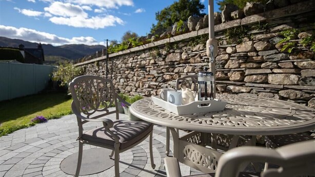 Une terrasse extérieure avec un mur en pierre, une table ronde en métal et deux chaises.