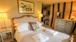A neatly made bed with pillows and folded towels, a bedside table with a lamp, a dresser with drawers, and a framed picture on the wall. - Low Cartmell Fold (Kendal)