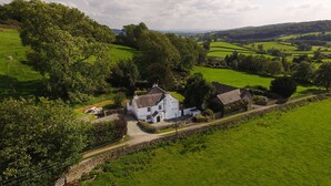 A rural house with a stone wall, surrounded by lush green fields and trees. - Low Cartmell Fold (Kendal)