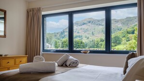 A hotel room with a bed, a wooden dresser, a window with a mountain view, and a curtain. - The Old Police House (Ambleside)