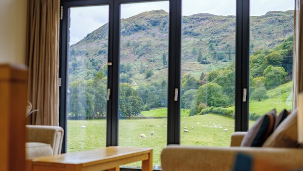 A room with a large sliding glass door leading to a grassy field with sheep. - The Old Police House (Ambleside)