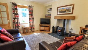 Una sala de estar con chimenea, sofás de cuero, televisor y estantería.