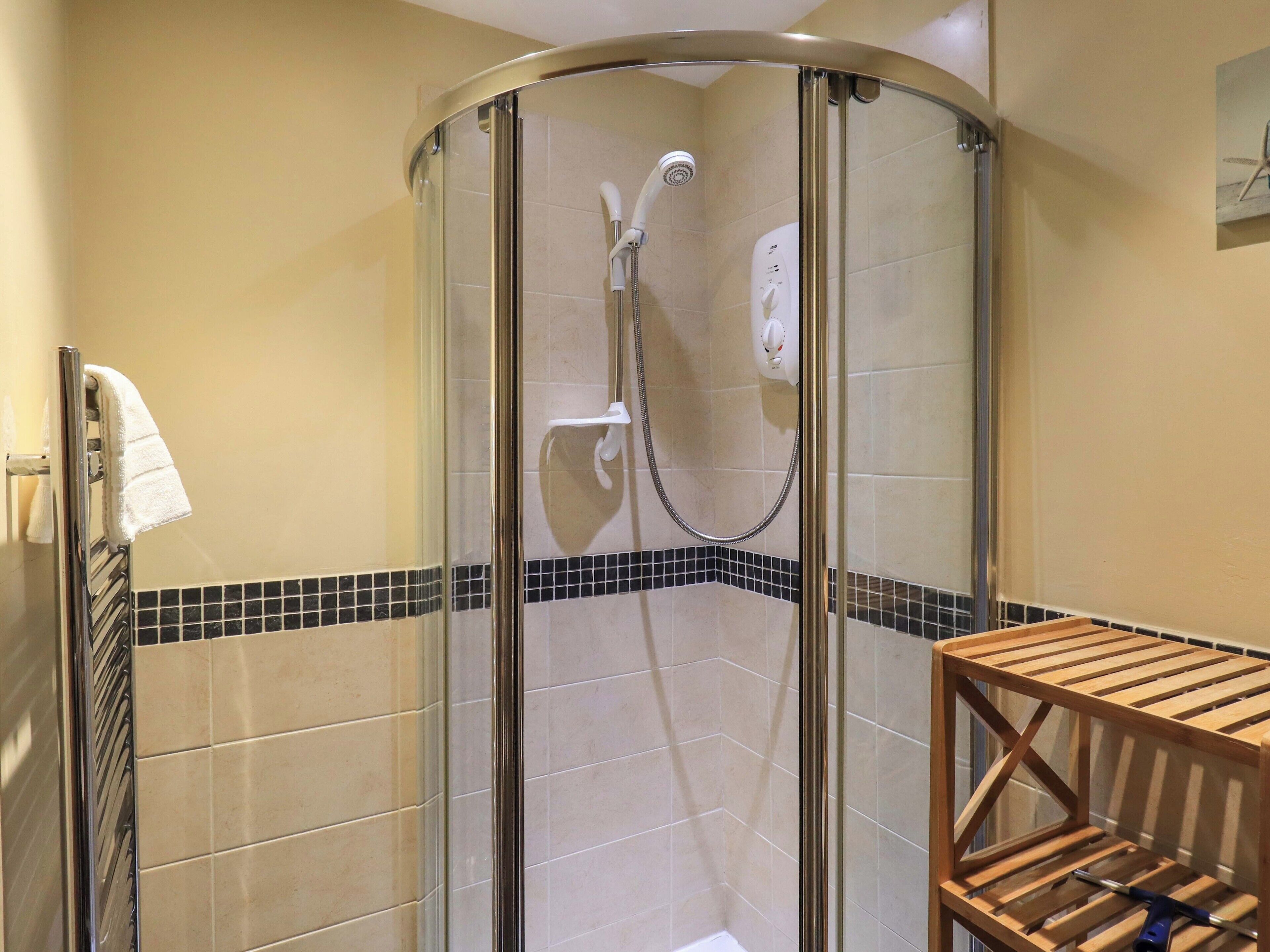 A glass-enclosed shower with a handheld showerhead and a wall-mounted control panel.