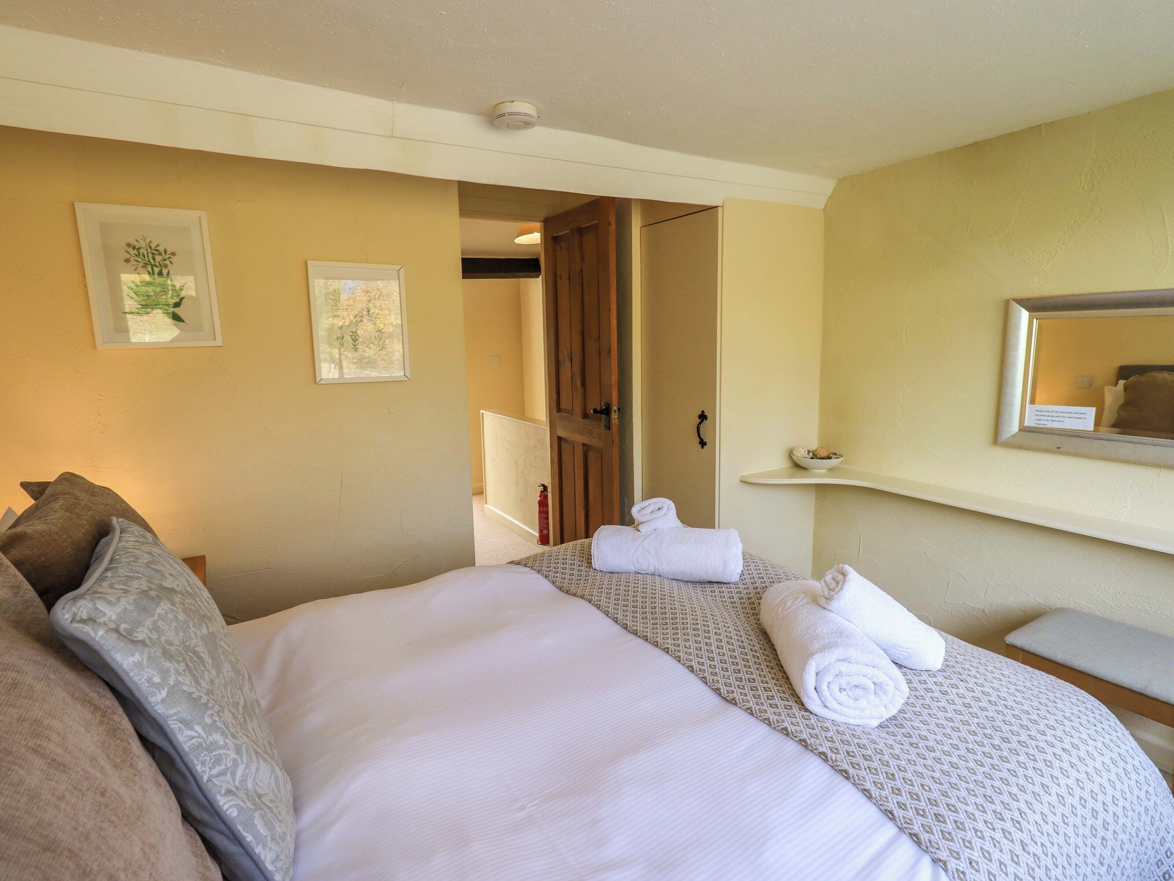 A hotel room with a bed, a bedside table, a mirror, and a door leading to another room.