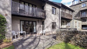 A two-story building with a balcony, a stone wall, and a paved patio area with outdoor furniture. - Gillybeck (Ambleside)