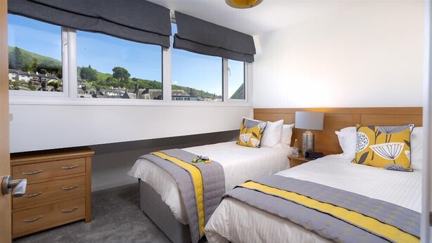 Une chambre d’hôtel avec deux lits, une commode en bois, une fenêtre donnant sur la ville et une lampe sur la table de chevet.