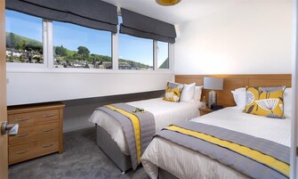 A hotel room with two beds, a wooden dresser, a window with a view of a town, and a lamp on the nightstand.